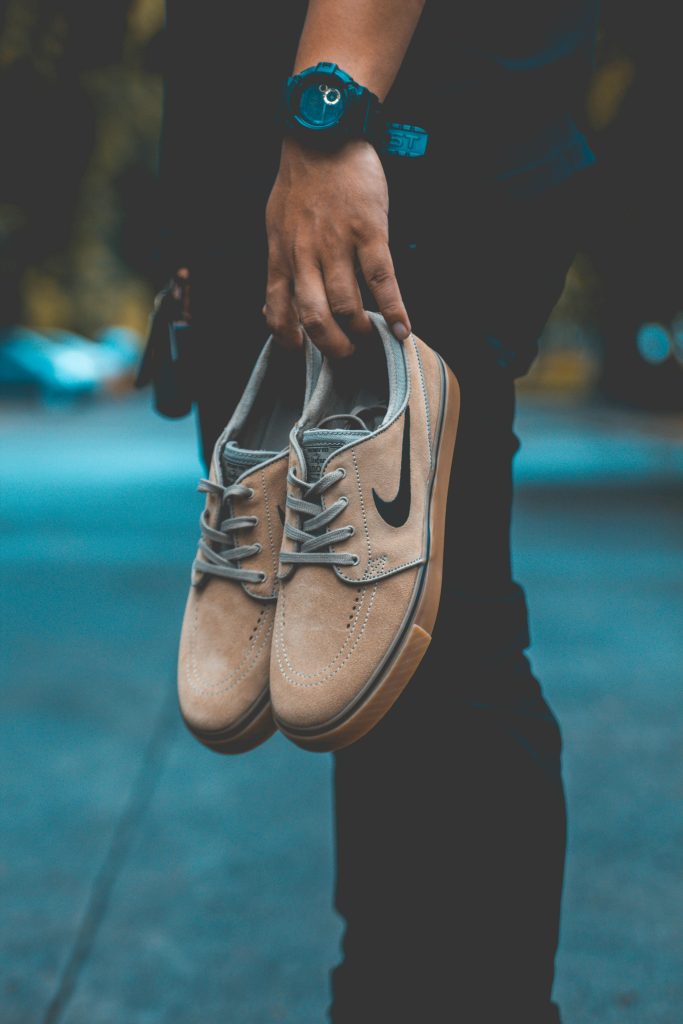 A person outdoors holding beige Nike sneakers, showcasing style and urban fashion.